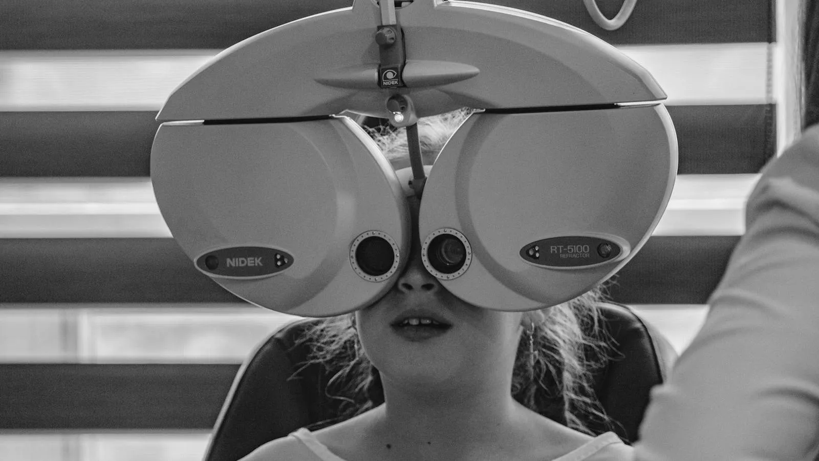 Referência de enquadramento: O exame acontecendo no consultório da optometrista. Horizontal, de ponta a ponta. Precisa ficar claro que é outro espaço, e não a loja — é a foto que sustenta a honestidade do bloco inteiro.