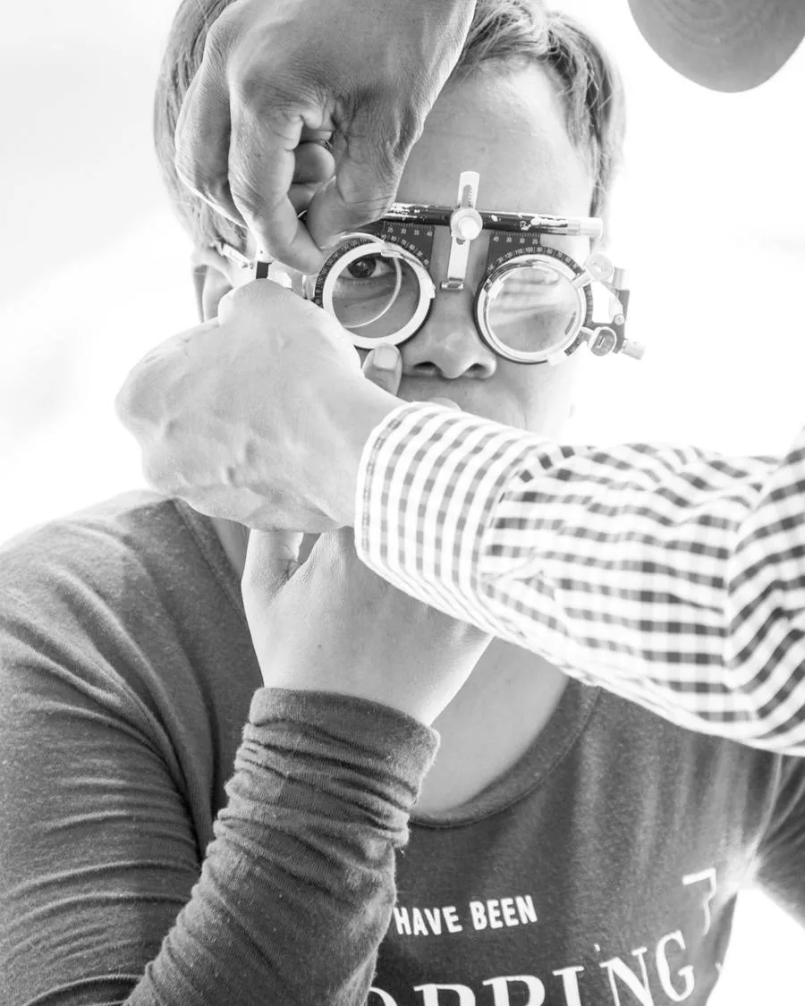 Referência de enquadramento: Retrato da optometrista no consultório dela. Em atendimento, com o equipamento de exame em uso.